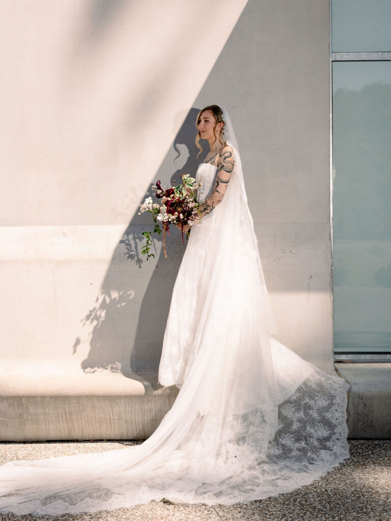 Bride in strapless lace gown holding dark trailing bouquet of calla lilies, clematis vine and blackberries at Bundanon Art Museum, Shoalhaven – wedding florals by Krysta Smith