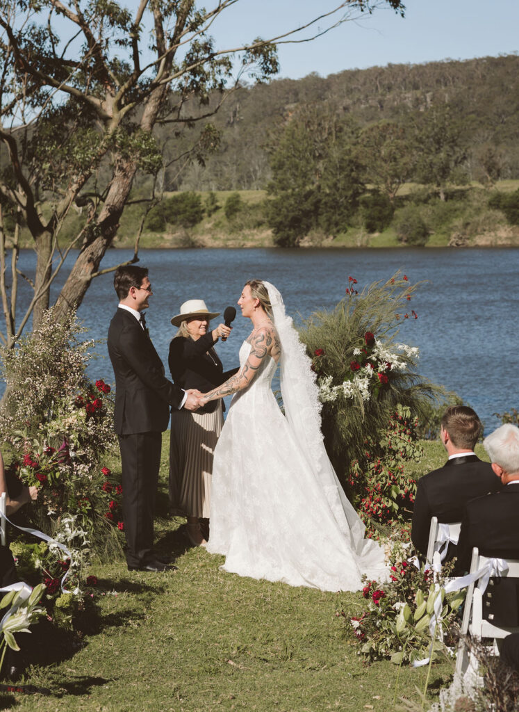 Bride and groom exchanging vows on the Shoalhaven River lawn at Bundanon Trust, flanked by sculptural foam-free floral towers and meadow-style aisle clusters – Bundanon wedding flowers by Krysta Smith
