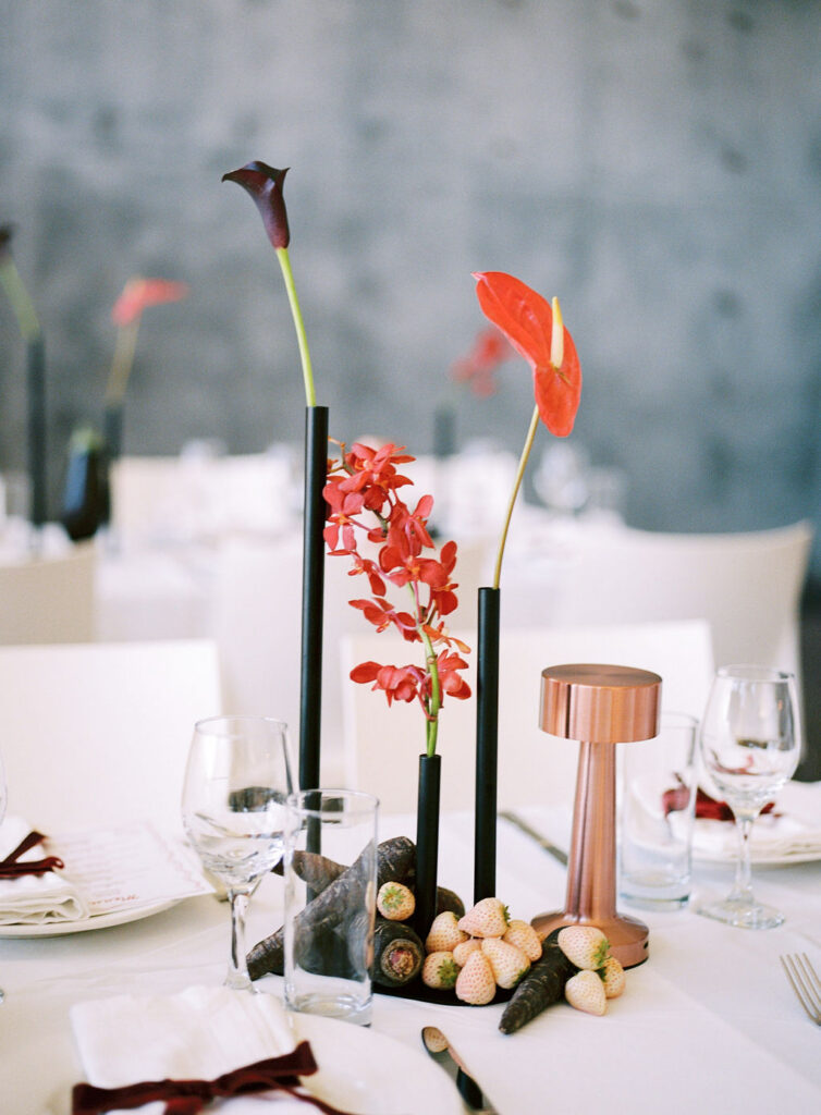 Sculptural Bundanon wedding reception tablescape with dark calla lily, red anthurium, black taper candles, copper lamp and artichokes inside the art gallery – Krysta Smith Floral Artistry